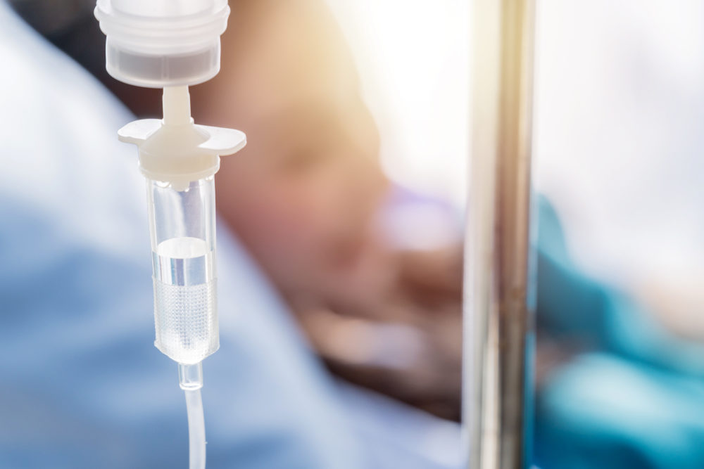 Closeup of the IV drip on the hanger with a patient in a hospital bed