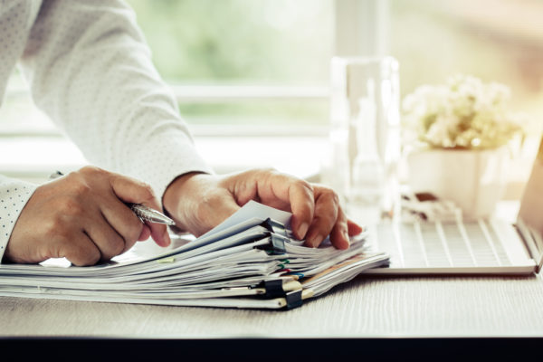 businessman holding a pen going through paperwork on desk by laptop