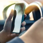 Young man reading messages holding a cell phone while driving.