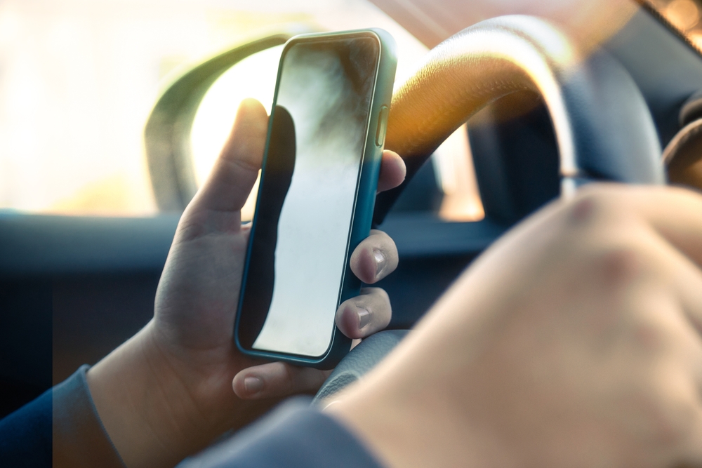 Young man reading messages holding a cell phone while driving.