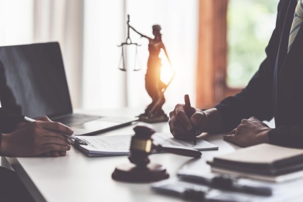 Business woman and lawyers discussing contract papers with brass scale on wooden desk in office.