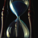 Old vintage wood frame blue sand hourglass countdown on dark background
