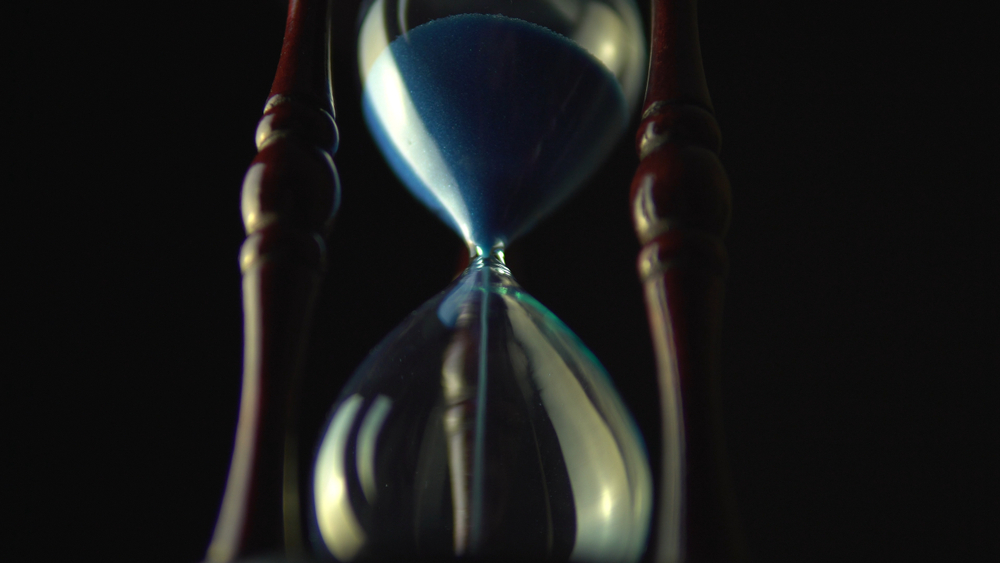 Old vintage wood frame blue sand hourglass countdown on dark background
