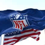 flag with the NFL logo waving in the wind with the US flag blurred in the background.