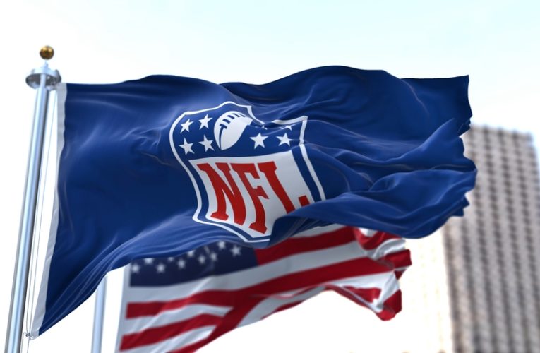 flag with the NFL logo waving in the wind with the US flag blurred in the background.