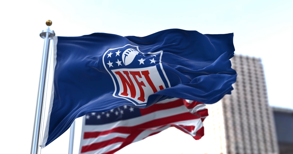 flag with the NFL logo waving in the wind with the US flag blurred in the background.