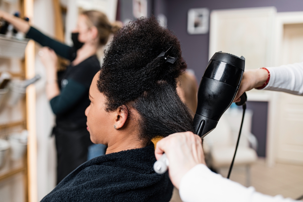 An middle aged African American woman on a curly hair straightening treatment at a hair salon.