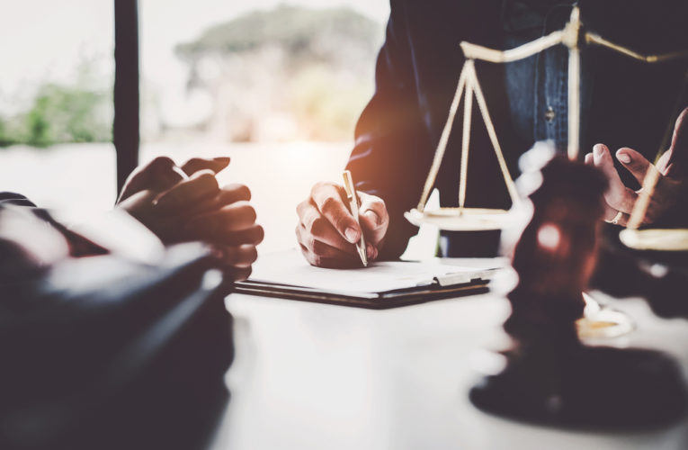 lawyers discussing contract papers with brass scale on wooden desk in office.