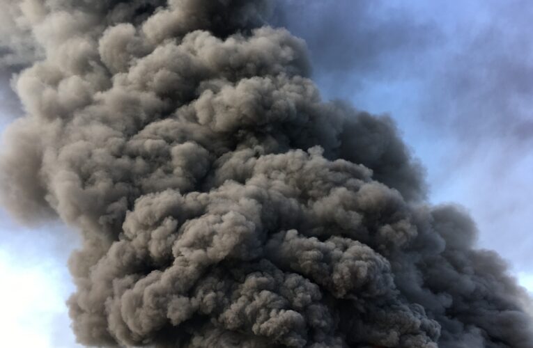 Warehouse engulfed in raging fire with huge column of smoke