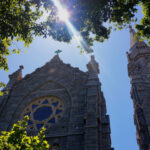 view of a catholic cathedral with the sun shining through trees above