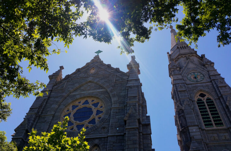 view of a catholic cathedral with the sun shining through trees above