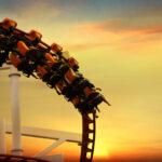 People on a roller coaster against a sunset background