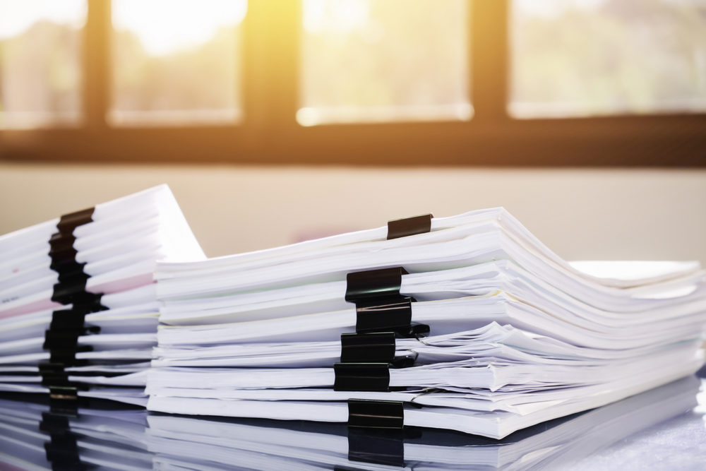 Stacks of papers bound with clips piled on a desk