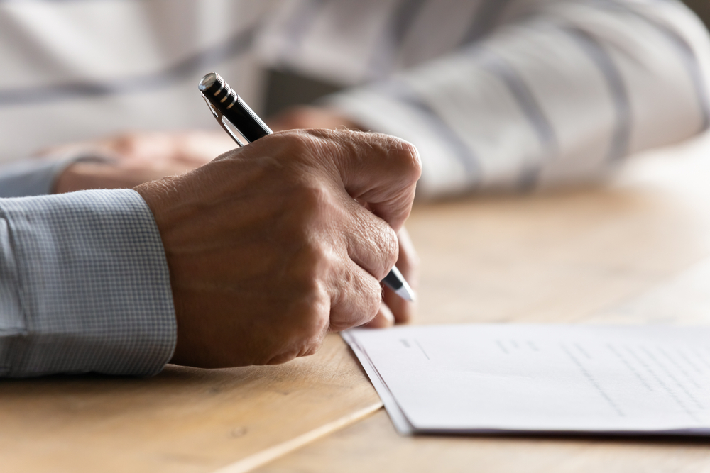 close up of an elderly mans hand signing a contract