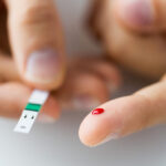 A drop of blood on a man's finger beside a test strip