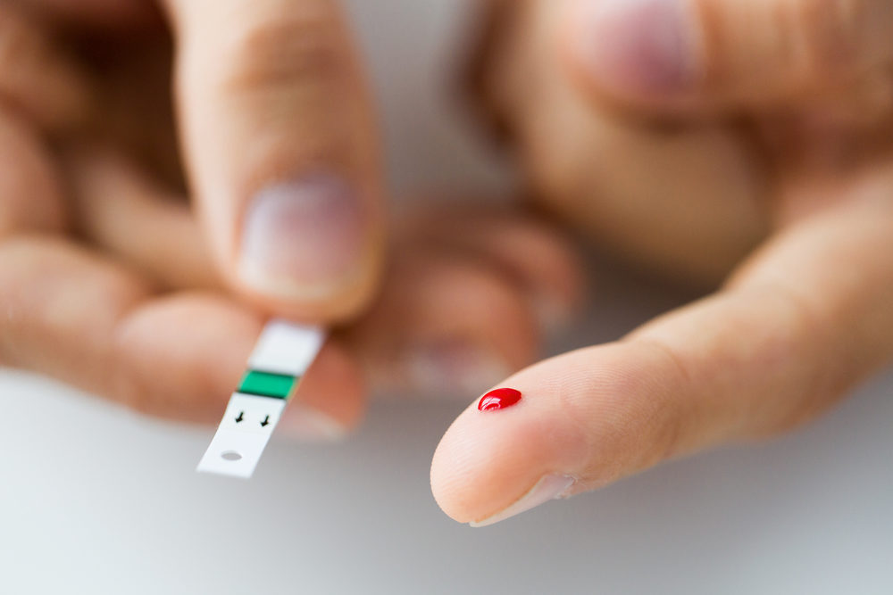 A drop of blood on a man's finger beside a test strip