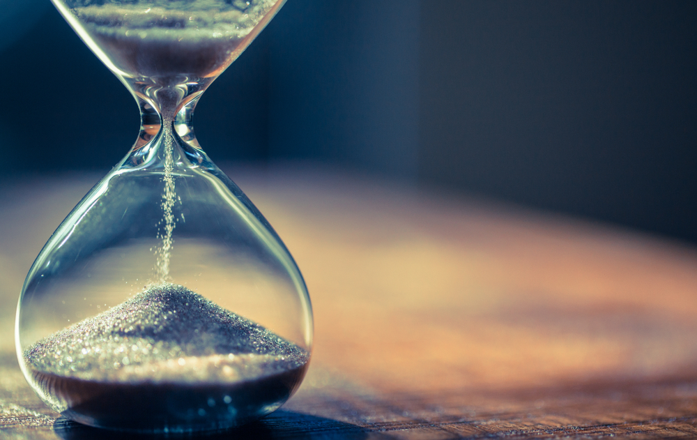 closeup of an hourglass with sand running through it on a wooden table