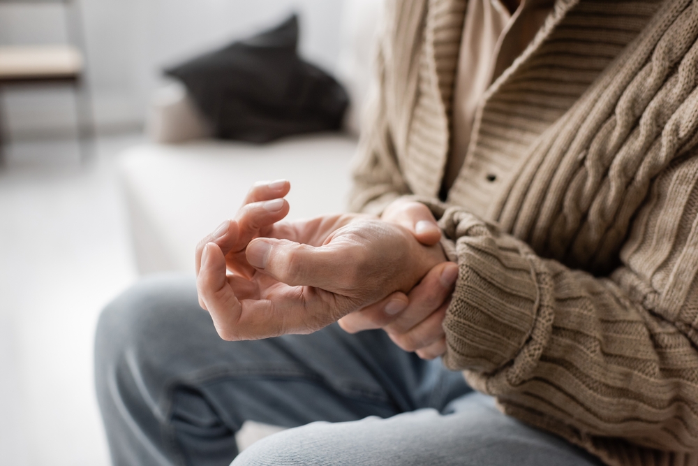 partial view of senior man with parkinsonism holding trembling hand while sitting at home