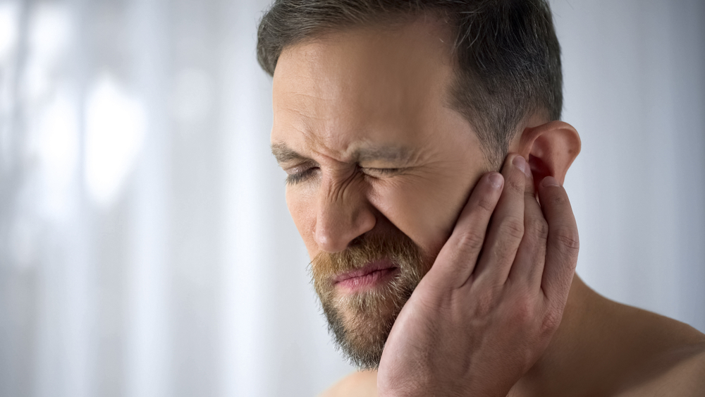 Man holding his aching ear, suffering from tinnitus, sudden hearing loss