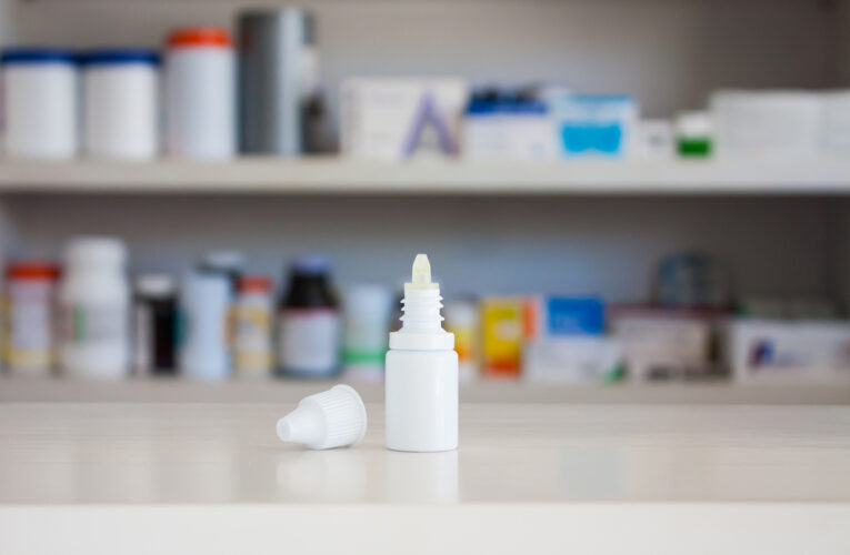 eye drop bottle on counter with medicine shelf blurred in background