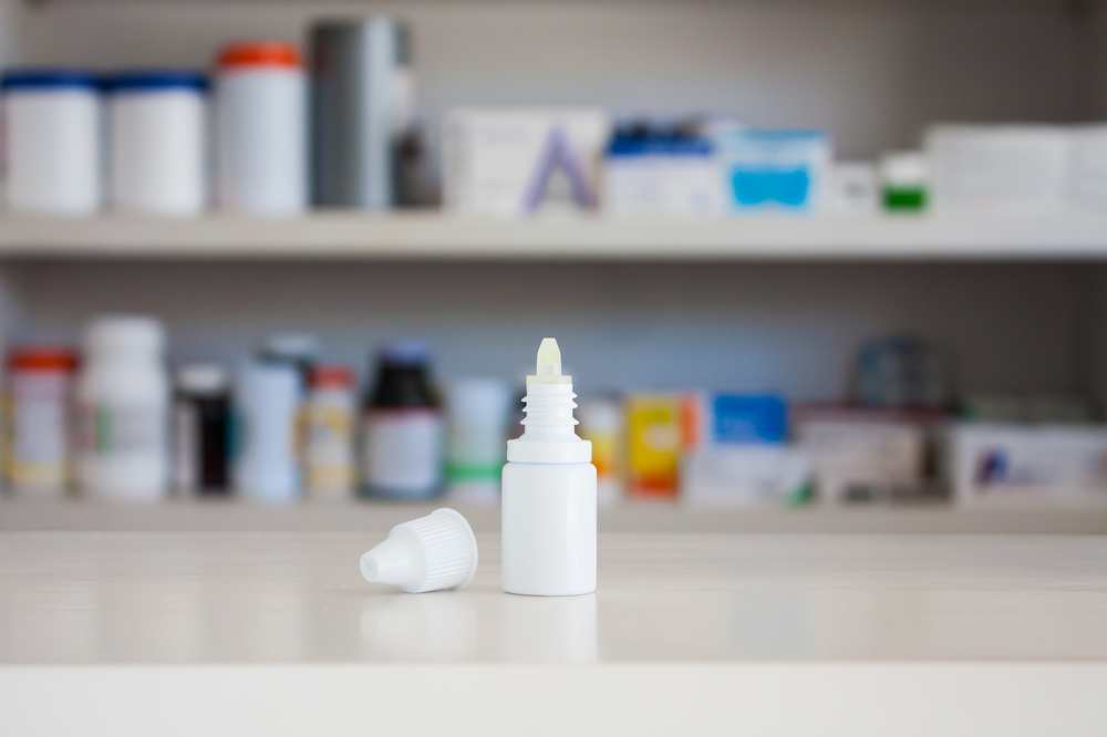 eye drop bottle on counter with medicine shelf blurred in background