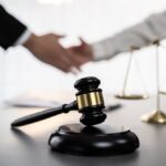 selective focus on gavel on an attorney's desk with blurred lawyer and client shaking hands