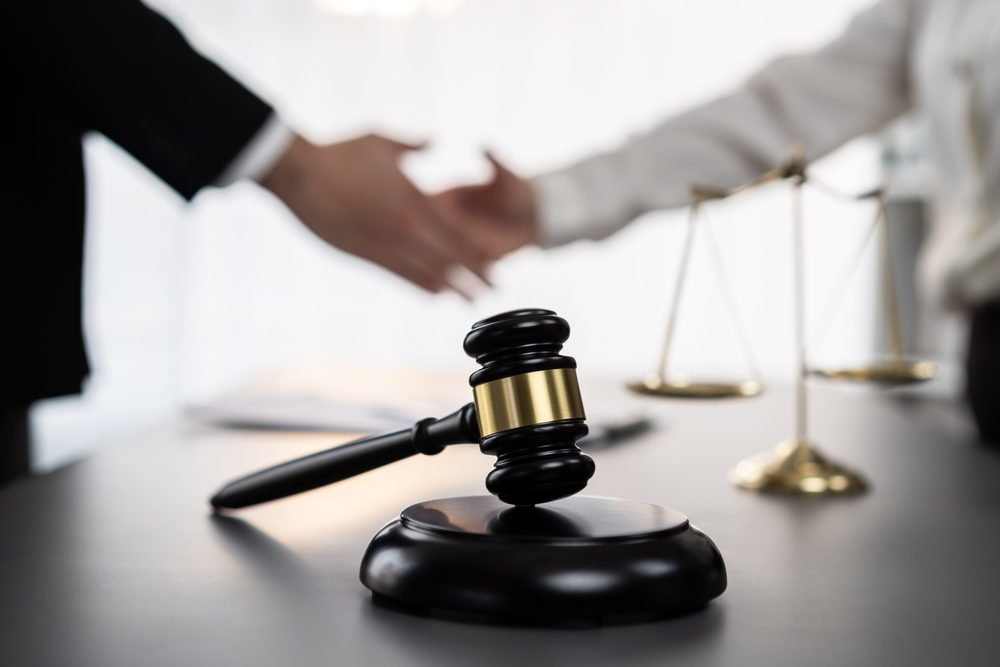 selective focus on gavel on an attorney's desk with blurred lawyer and client shaking hands