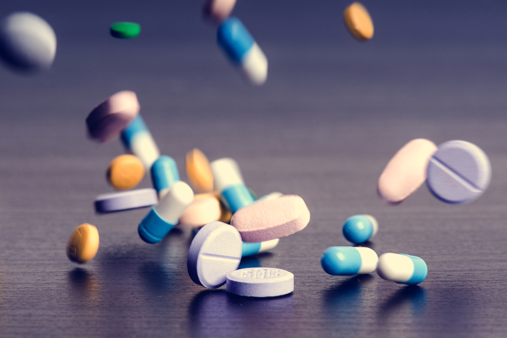 a variety of pills falling onto a dark wood table