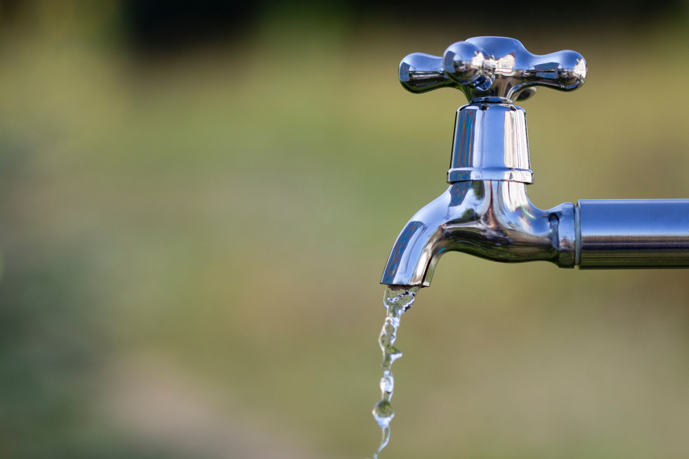 metal water faucet dripping water outside with blurred nature background