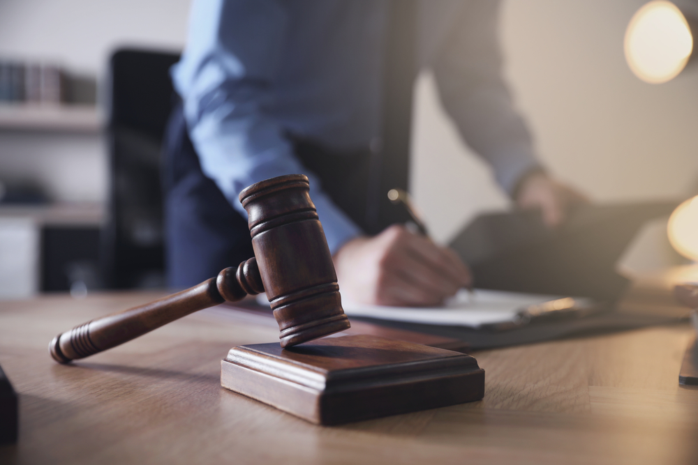 male lawyer writing at his desk with a wooden gavel in the forefront