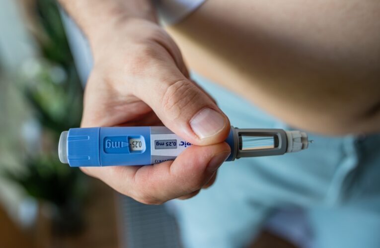 man holding an ozempic semaglutide pen to inject into his stomach