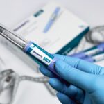Hands in blue surgical gloves holding Ozempic Insulin injection pen for diabetics.