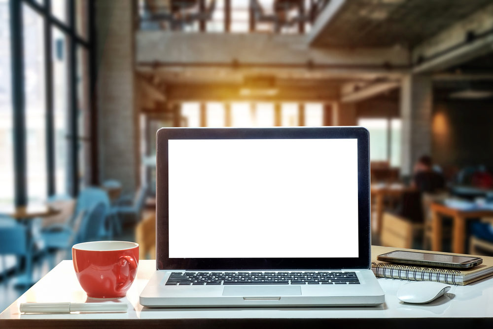 a blank screen on a laptop at a desk with coffee mug, mouse notepad, and phone